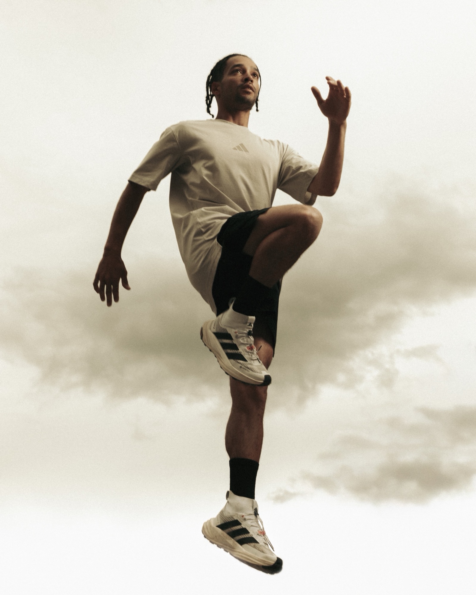 Adidas Terrex athlete performing a high-knee running drill beneath a cloudy sky